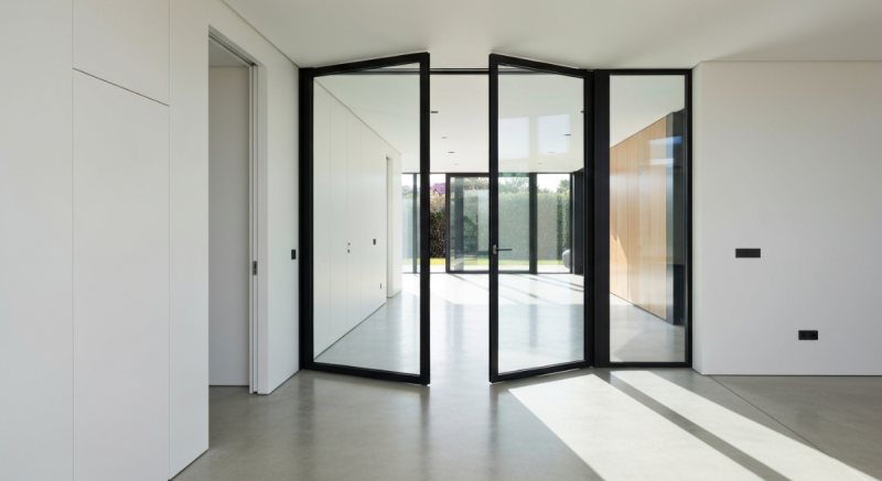 Porte pivot intérieure vitrée minimaliste VIEWFRAME avec cadres noirs ultra-fins dans une villa de luxe.